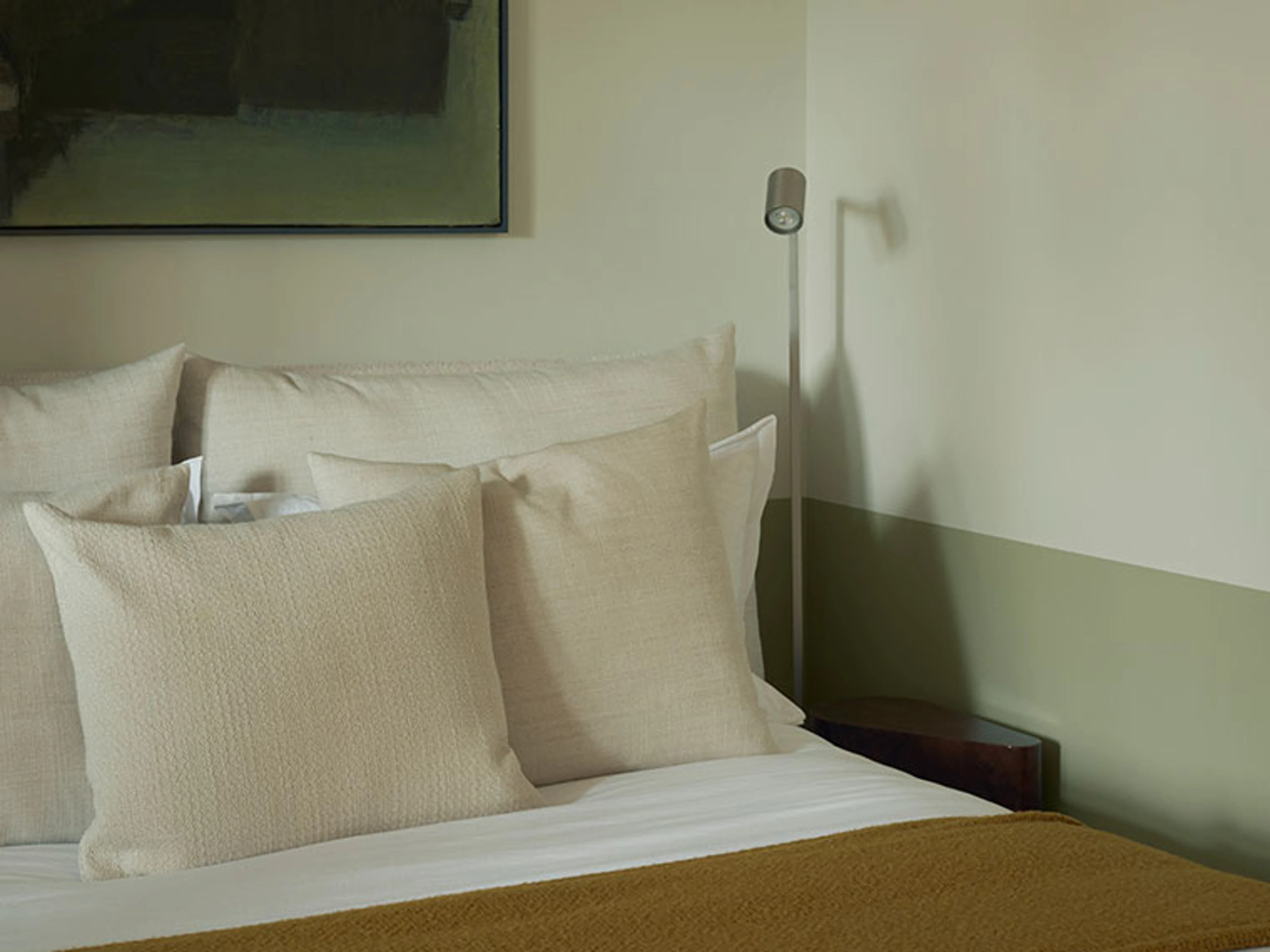 Detail of a made bed with cream-colored pillows, a mustard yellow throw, and a wall in muted shades of green.