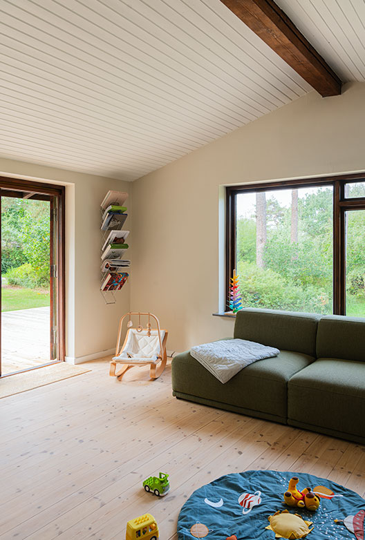 Bright living room with beige walls, a white ceiling with a dark beam, a green sofa and a large window facing the garden.