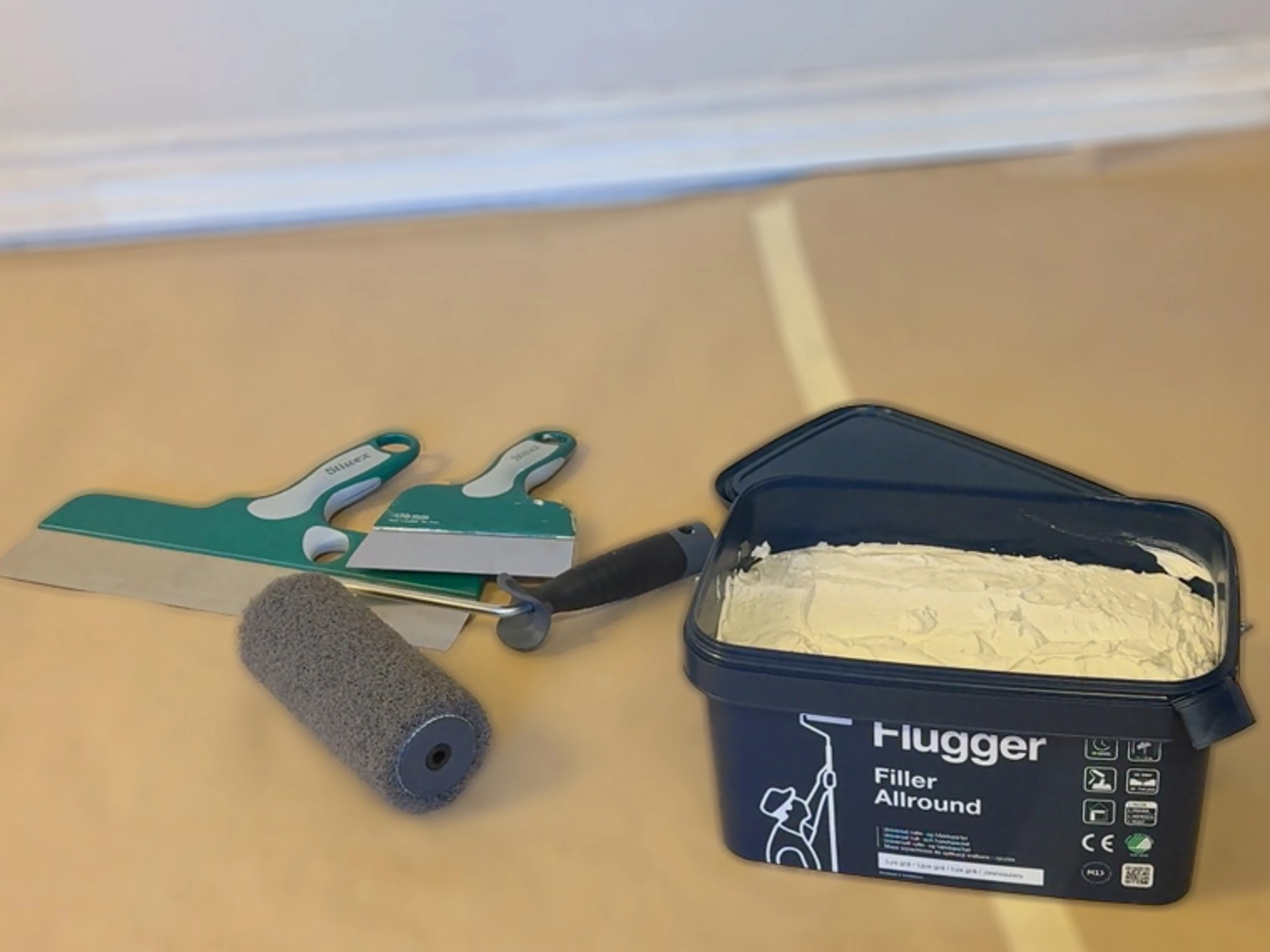Flügger Filler Allround med skumroller, spacklar och målarverktyg på täckpapp.