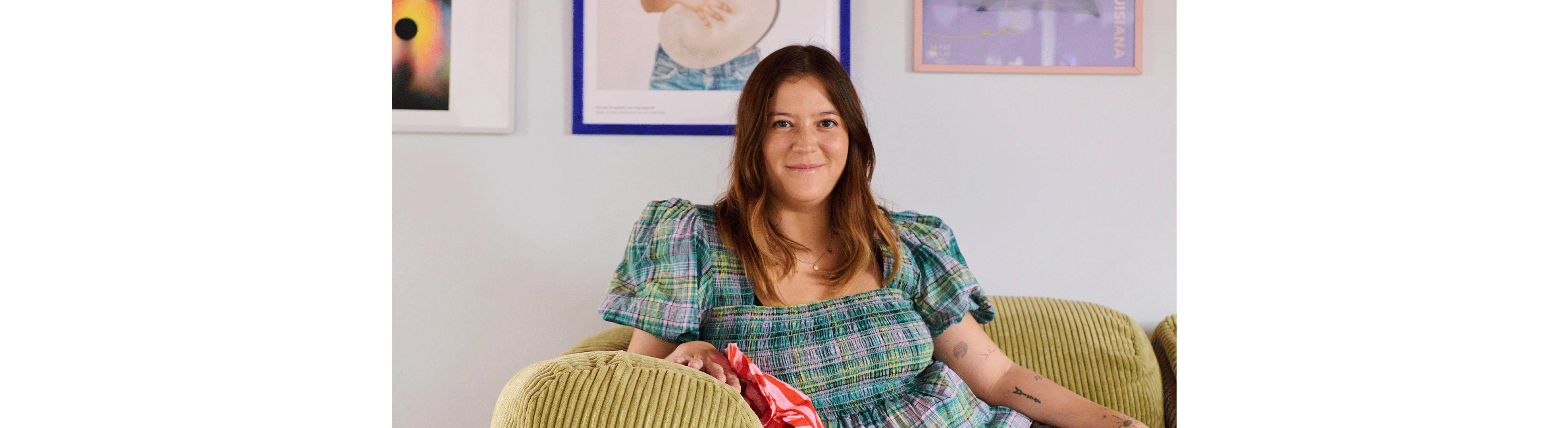 Belinda kigger ind i kameraet mens hun læner sig op armlænet på sofaen.