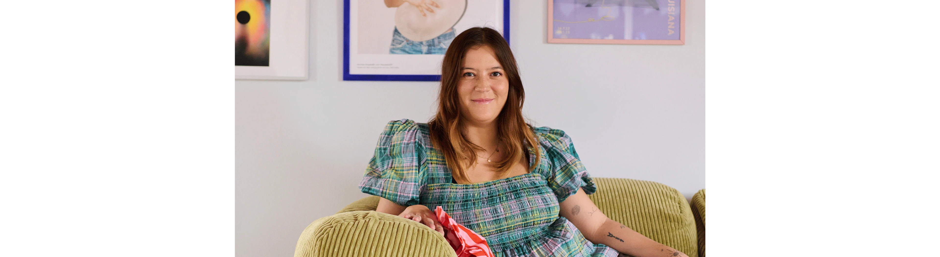 Belinda kigger ind i kameraet mens hun læner sig op armlænet på sofaen.