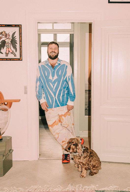 Smilende mand står i en døråbning med en brun hund siddende foran sig.