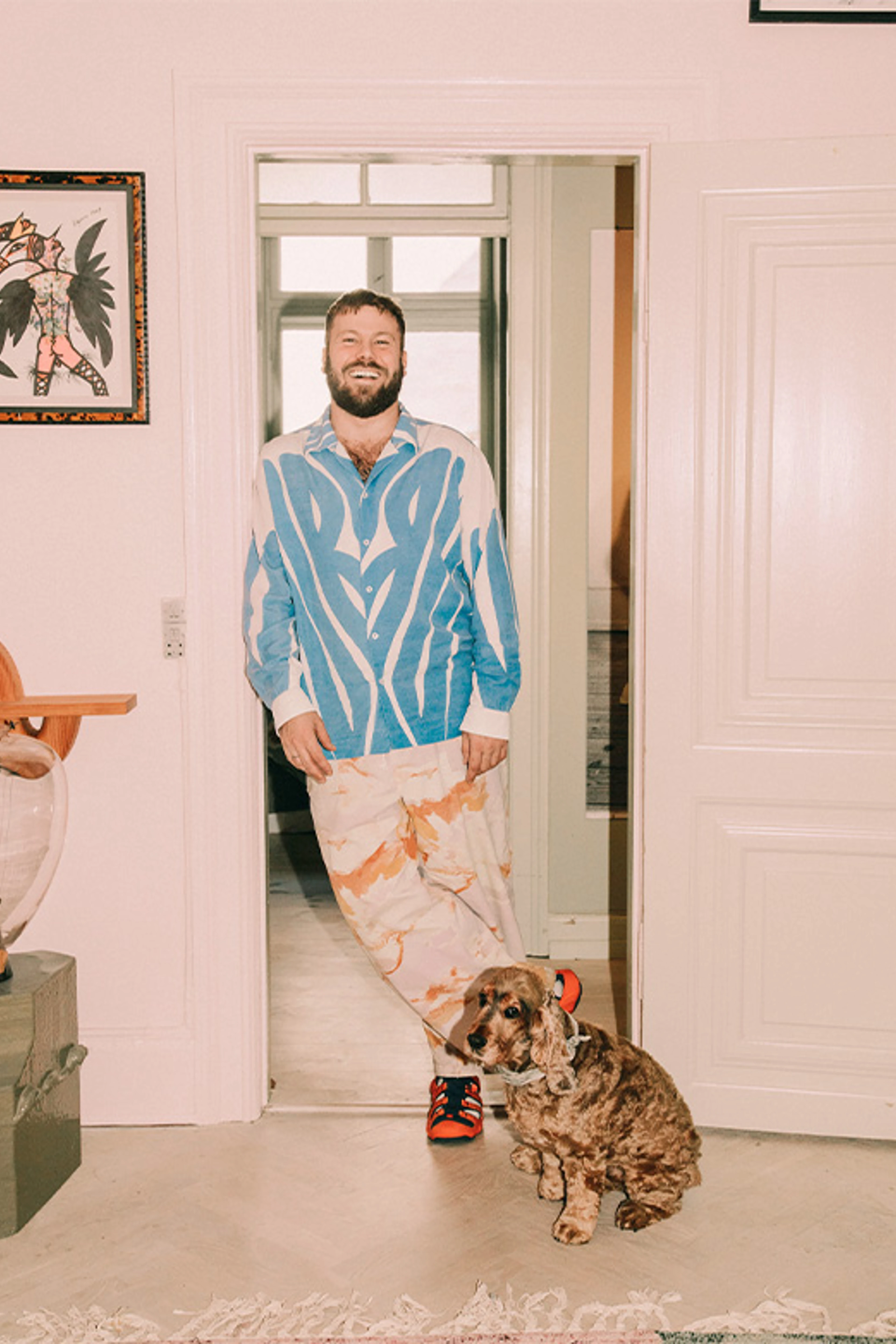 Smilende mand står i en døråbning med en brun hund siddende foran sig.