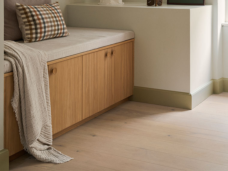 Beige fodpanel med en bænk i egetræ, ternet pude og strikket plaid.