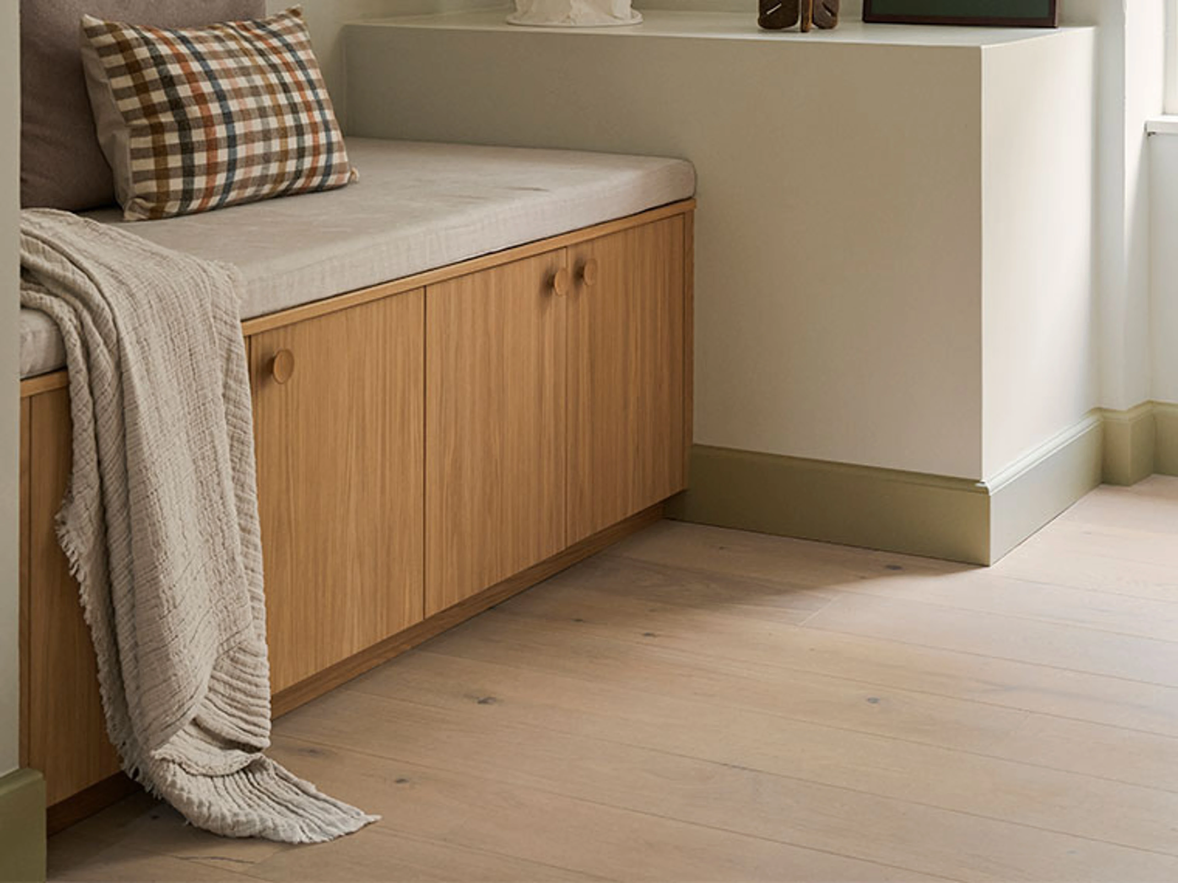 Beige fodpanel med en bænk i egetræ, ternet pude og strikket plaid.