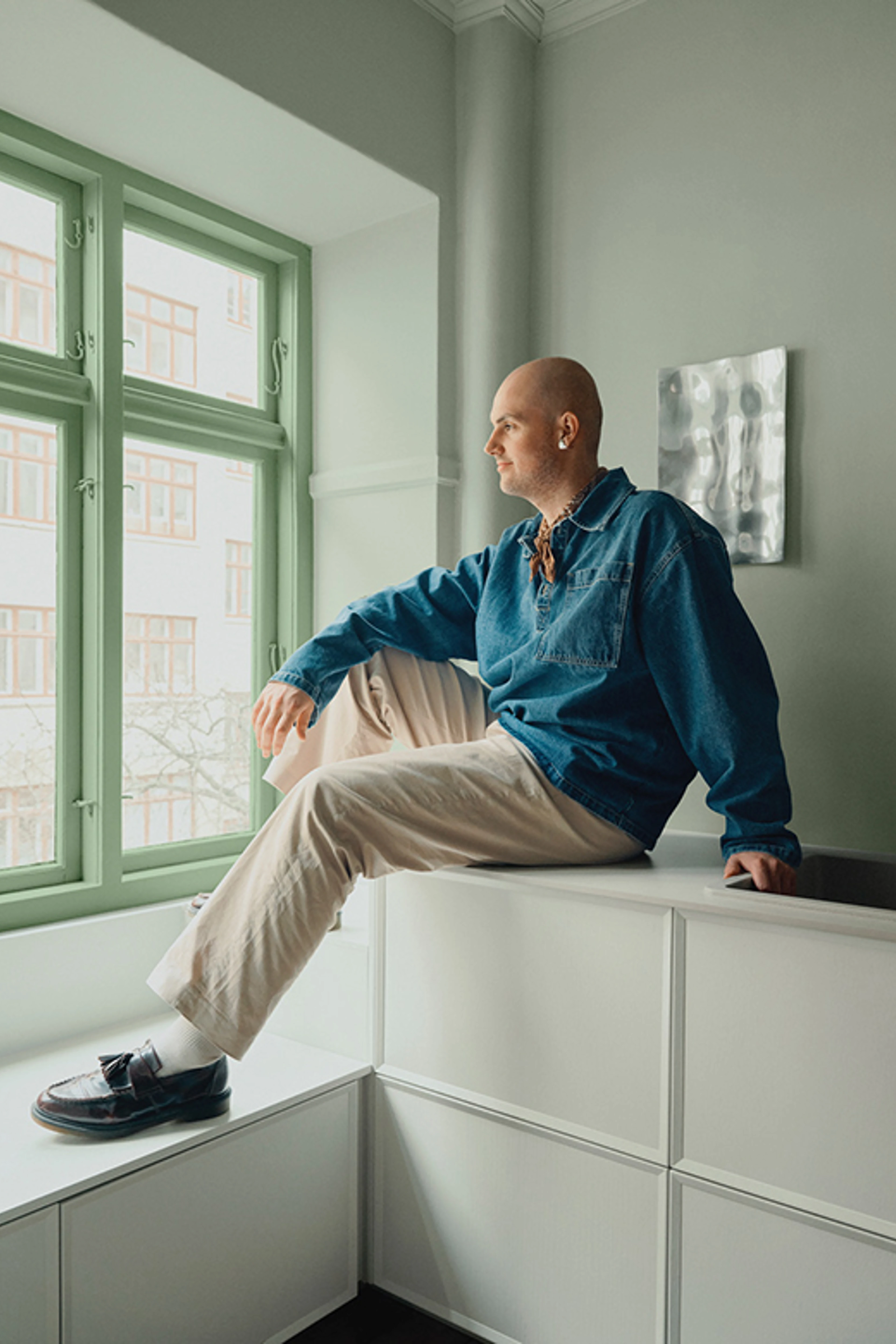 Nicolai sidder i en vinduesniche med grønne paneler, omgivet af lyse vægge og en rolig, afstemt farvepalette.