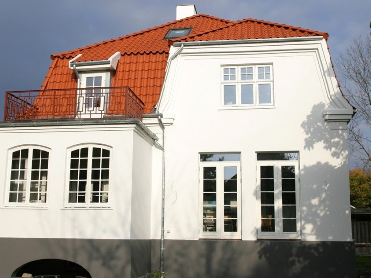 Renovert hus med nymalt hvit fasade, hvitinnrammede vinduer og rødt tegltak.