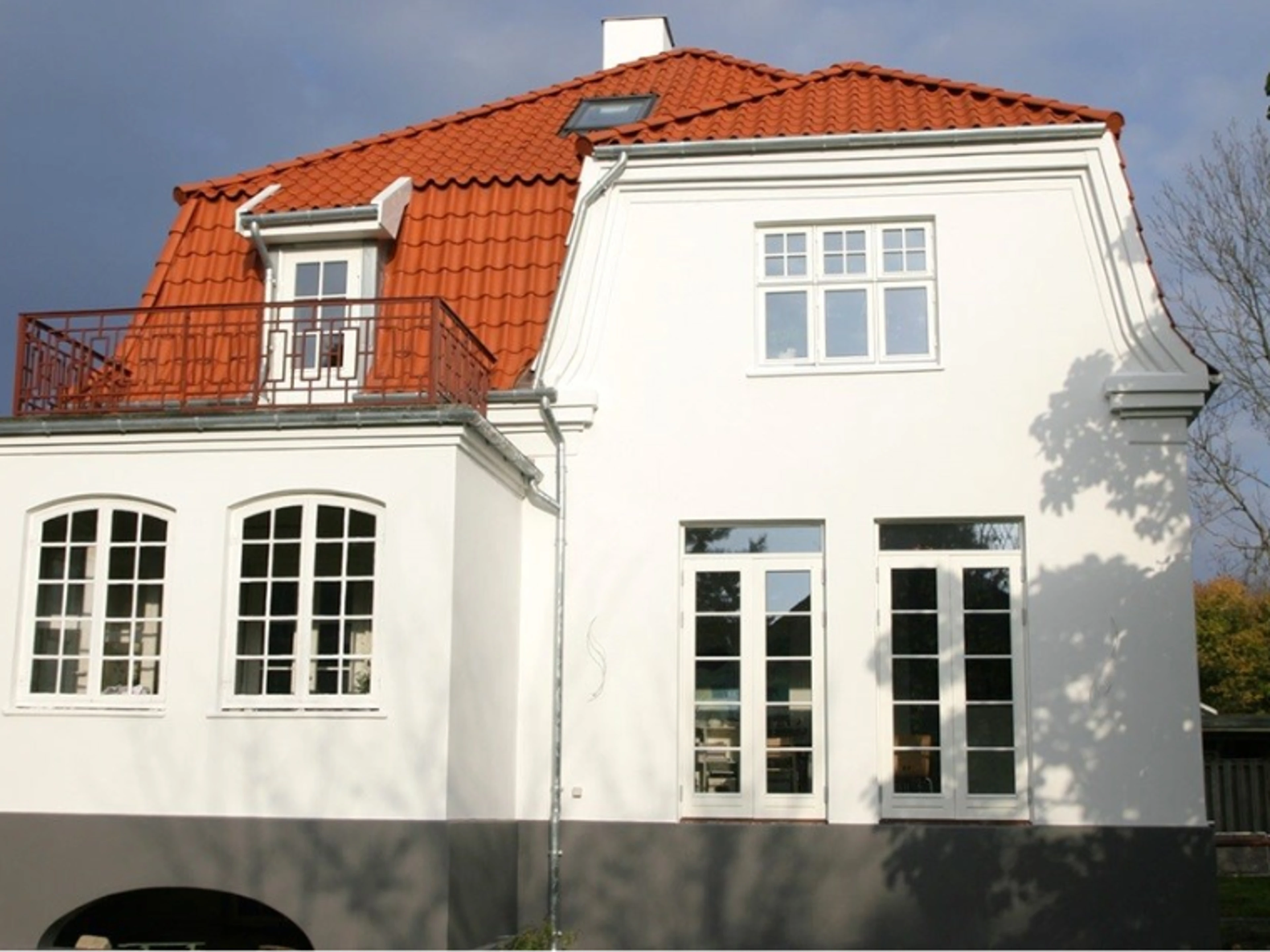 Renovert hus med nymalt hvit fasade, hvitinnrammede vinduer og rødt tegltak.