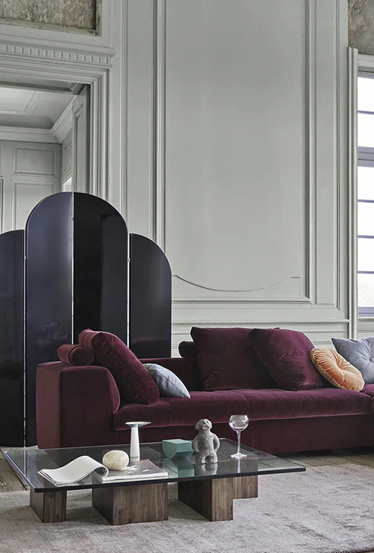 Stue med grå vegger, en bordeauxfarget sofa og et stuebord med glassplate og trebein.