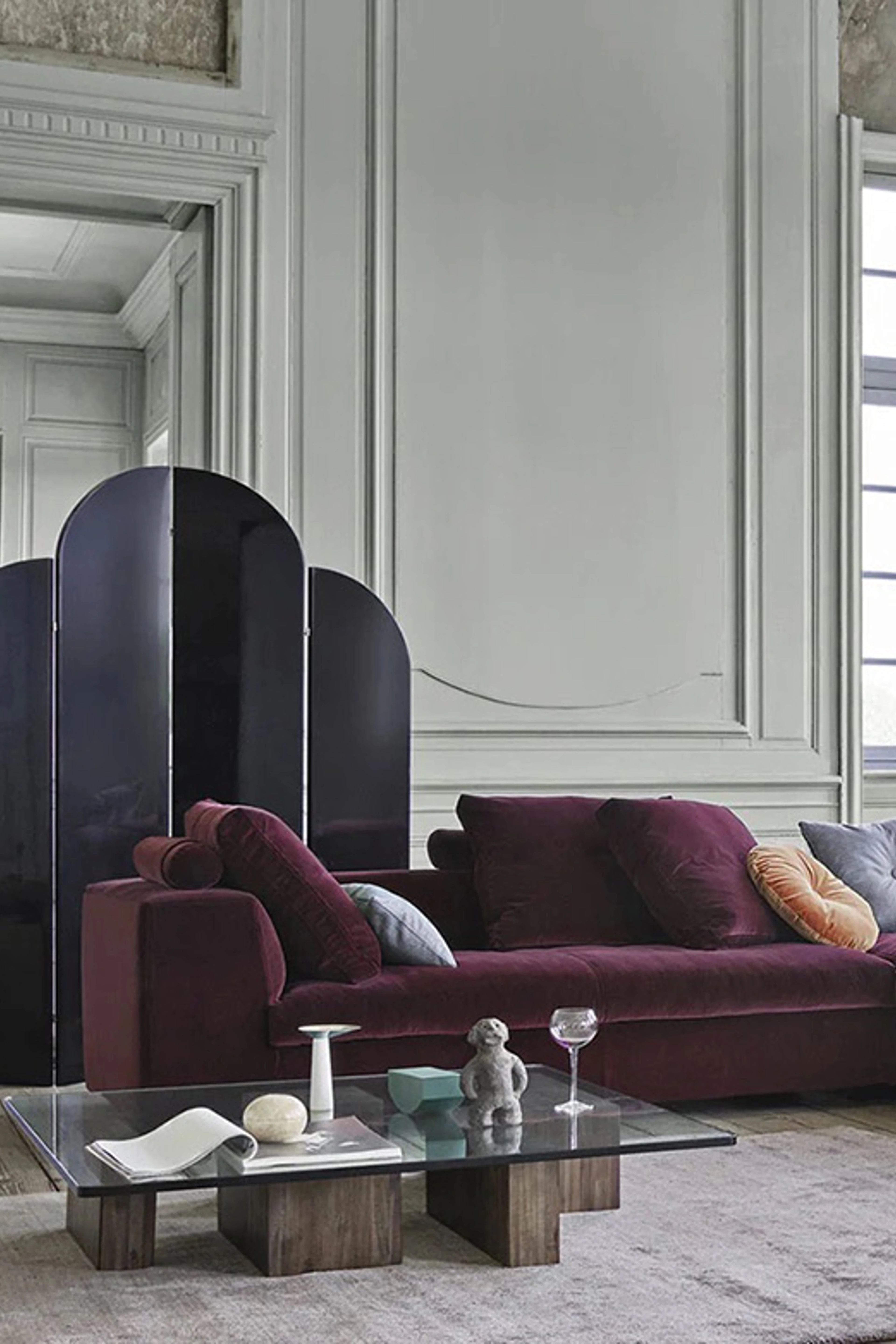 Stue med grå vegger, en bordeauxfarget sofa og et stuebord med glassplate og trebein.
