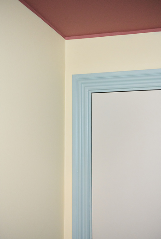 Detalje af rum med lyse vægge, rosa loft og dørkarm i lys blå nuance.