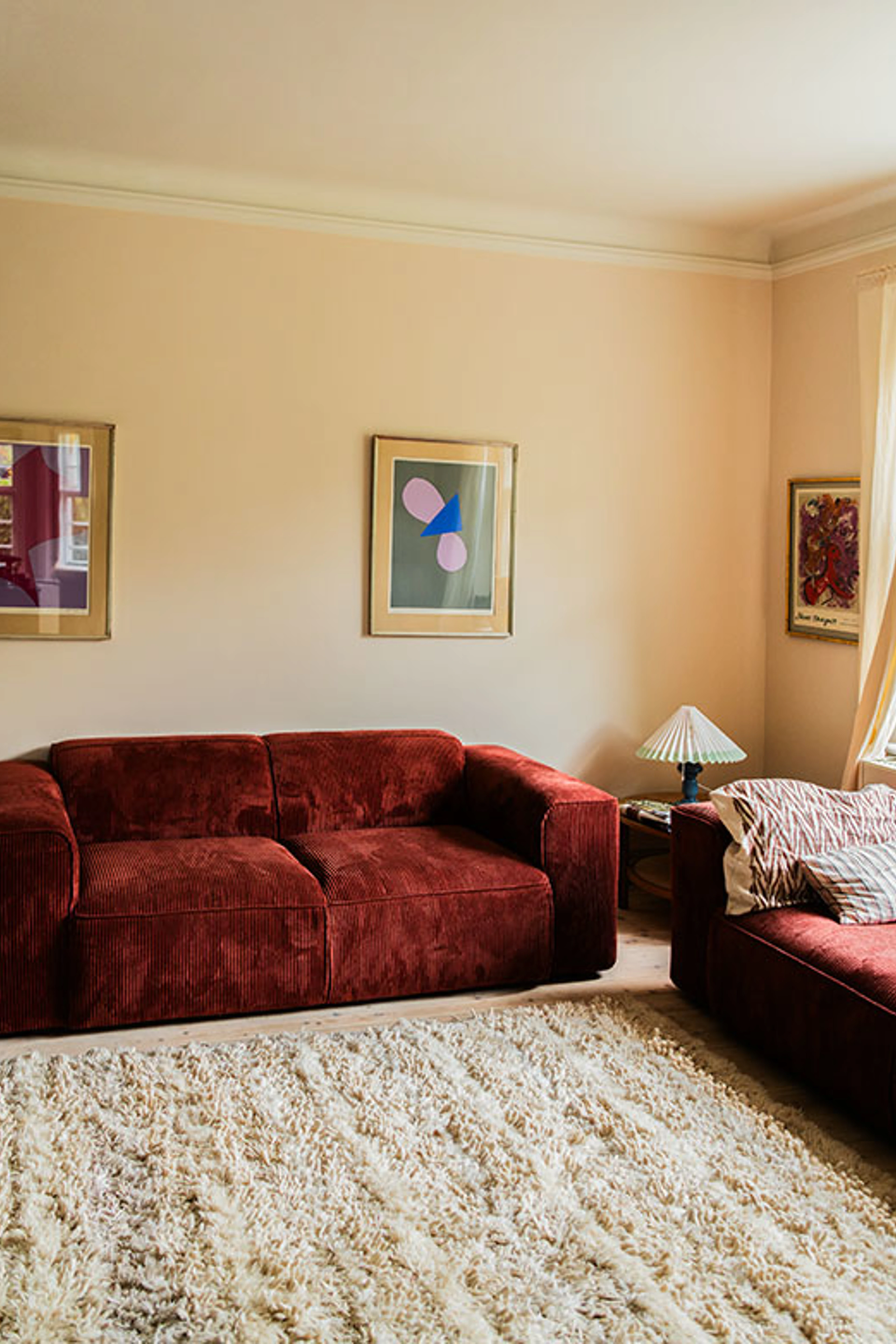 Stue med bordeaux sofa, lyst tæppe og kunst på væggene.