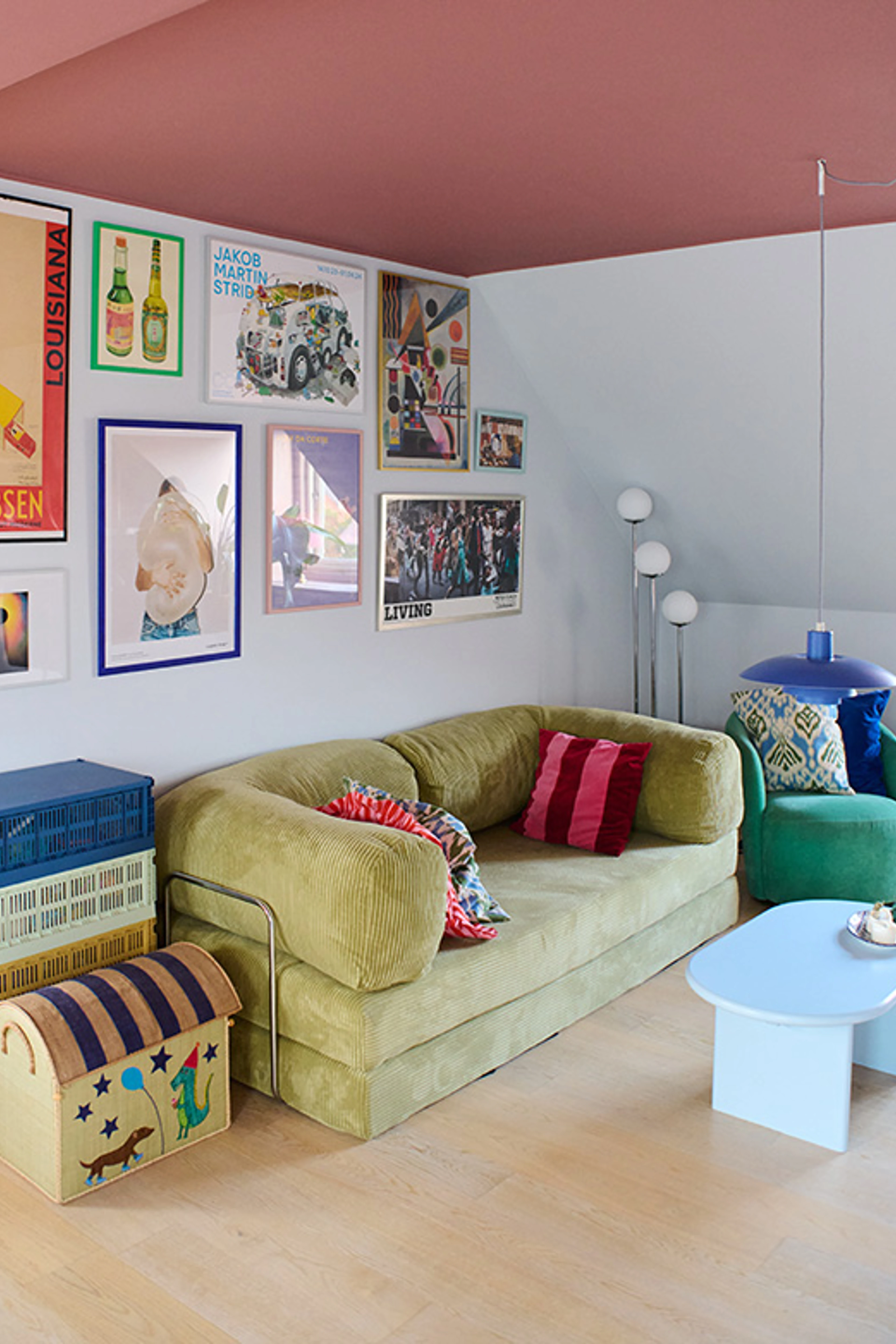 Stue med lyse vægge og rosa loft, indrettet med sofa, farverige puder, sofabord og væg med plakater.