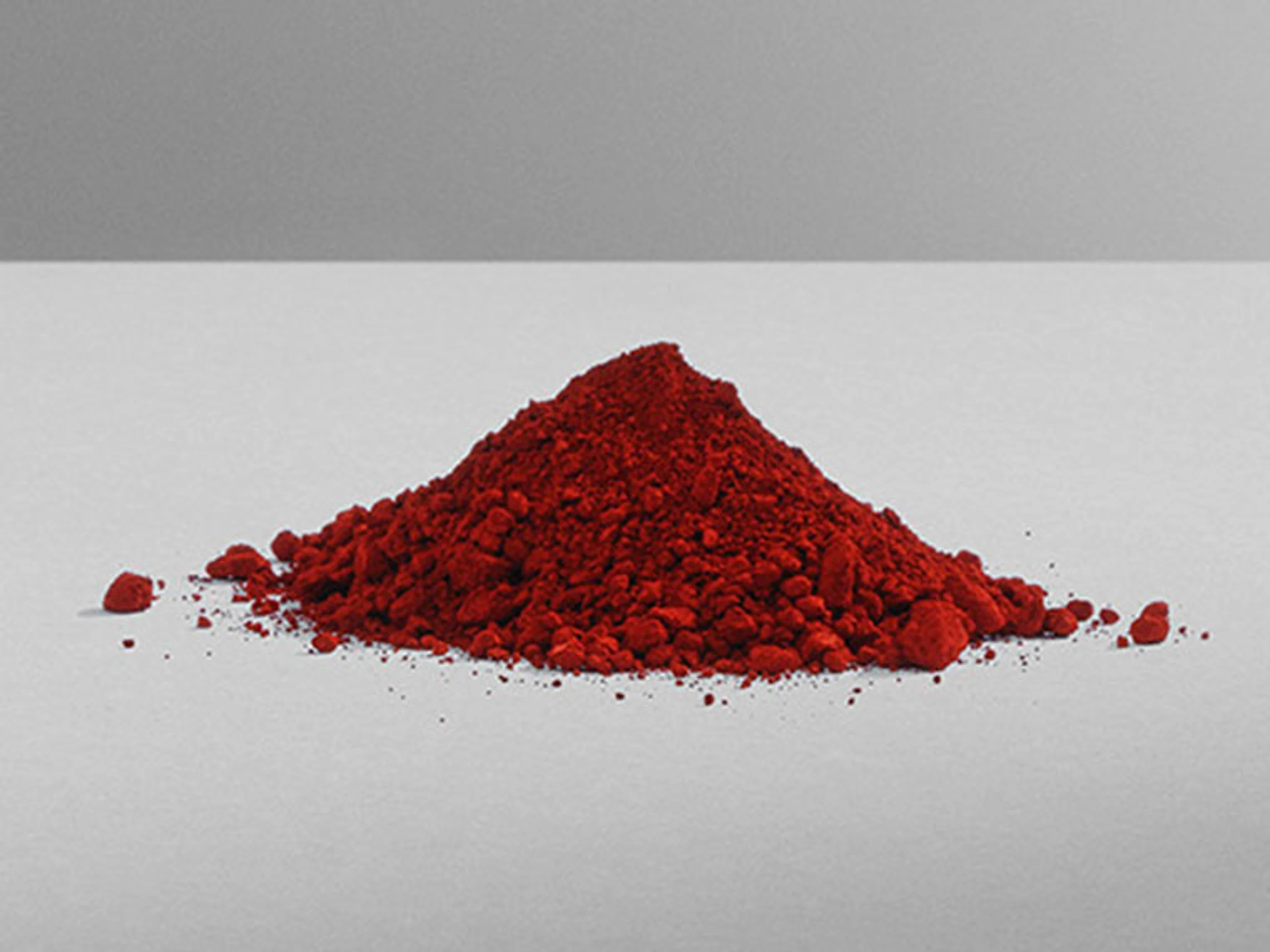 Hög med rött färgpigment på ljusgrå bakgrund, som illustrerar pigment som används vid tillverkning av färg.