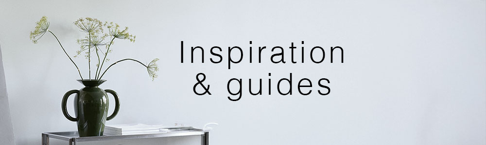 Vase med grønne blomster på et sidebord foran en lys væg med teksten "Inspiration & guides".