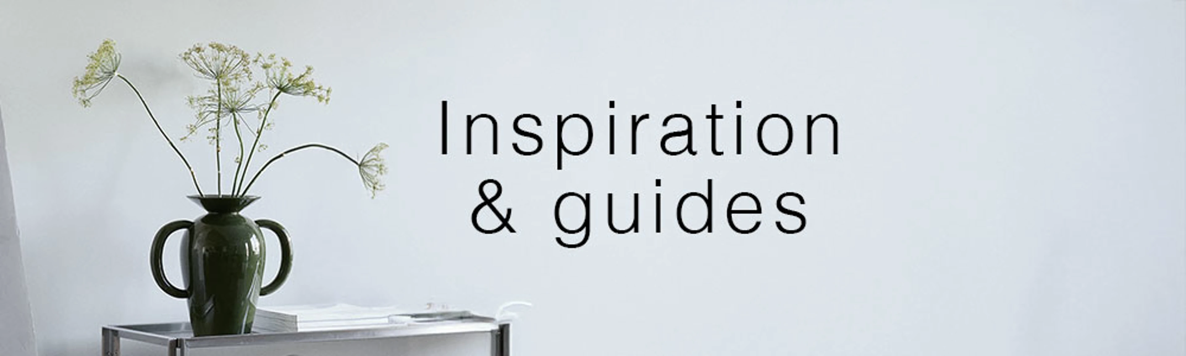 Vase med grønne blomster på et sidebord foran en lys væg med teksten "Inspiration & guides".