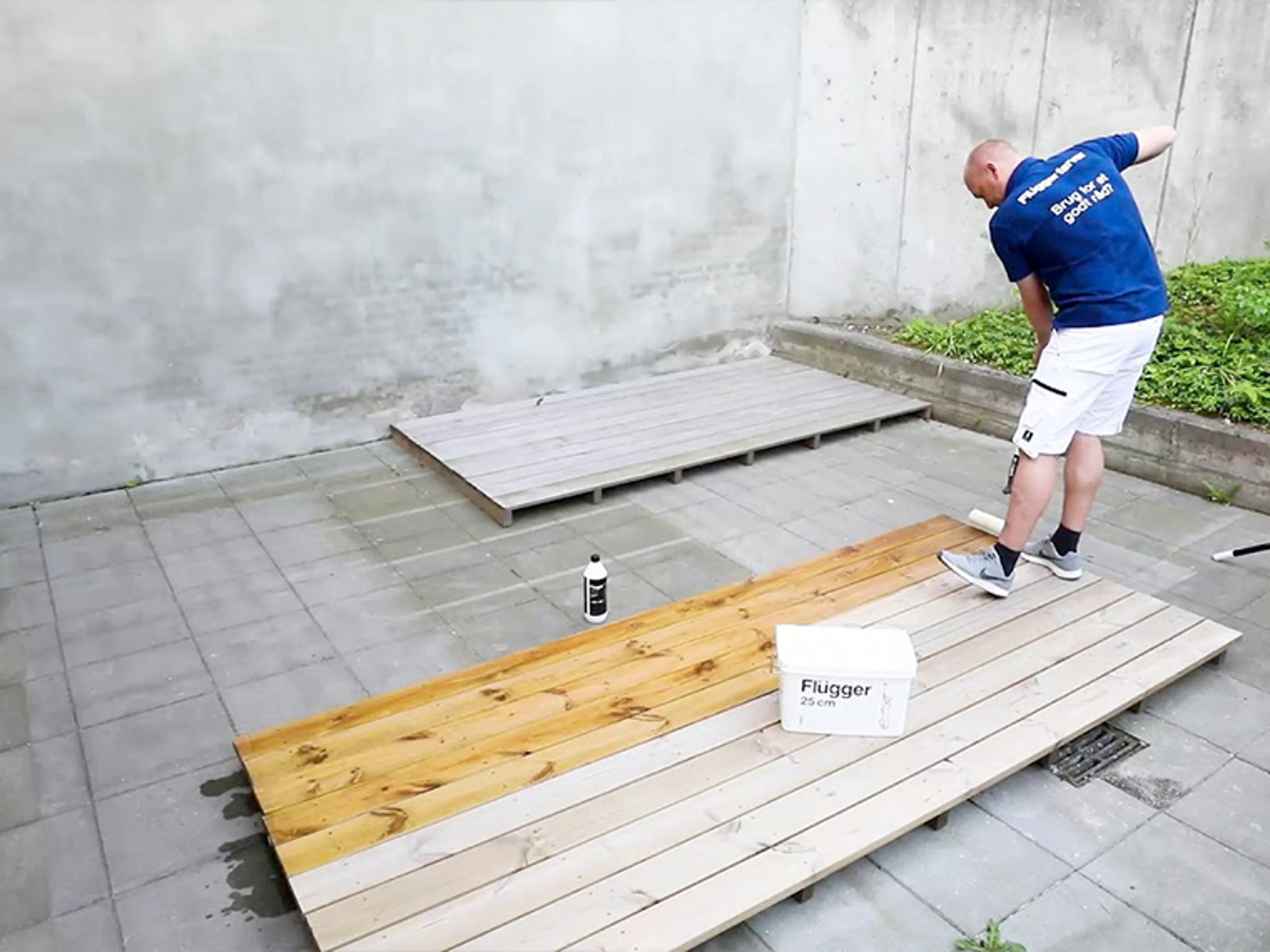 Person påfører treolje på terrassebord og viser forskjellen mellom ubehandlet og behandlet tre.