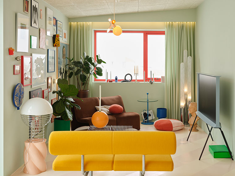 Colorful living room with a yellow sofa, brown armchair, mint green walls, artwork, plants, and a freestanding TV.