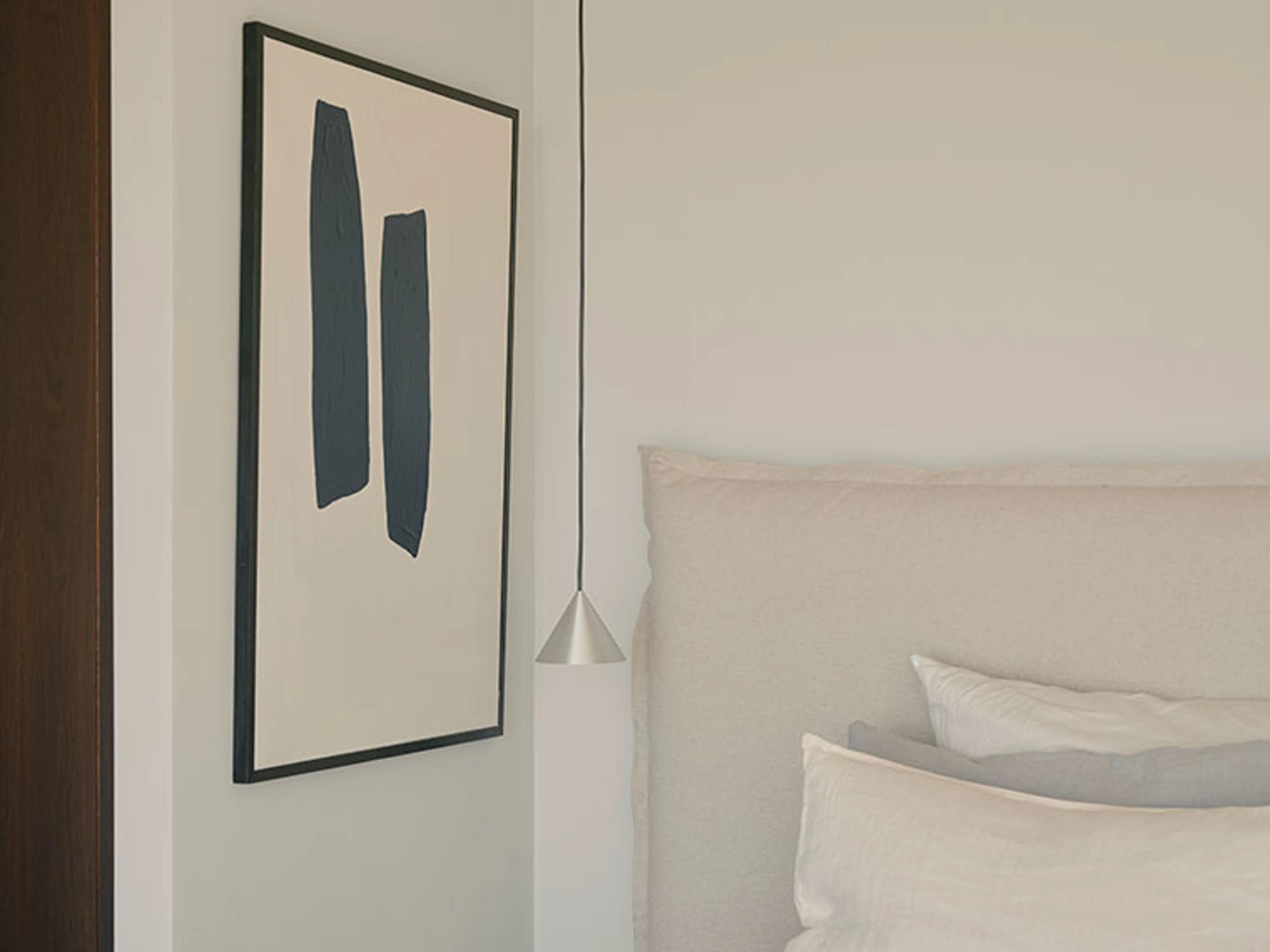 Soveværelse med polstret sengegærde, kunstplakat og pendellampe.