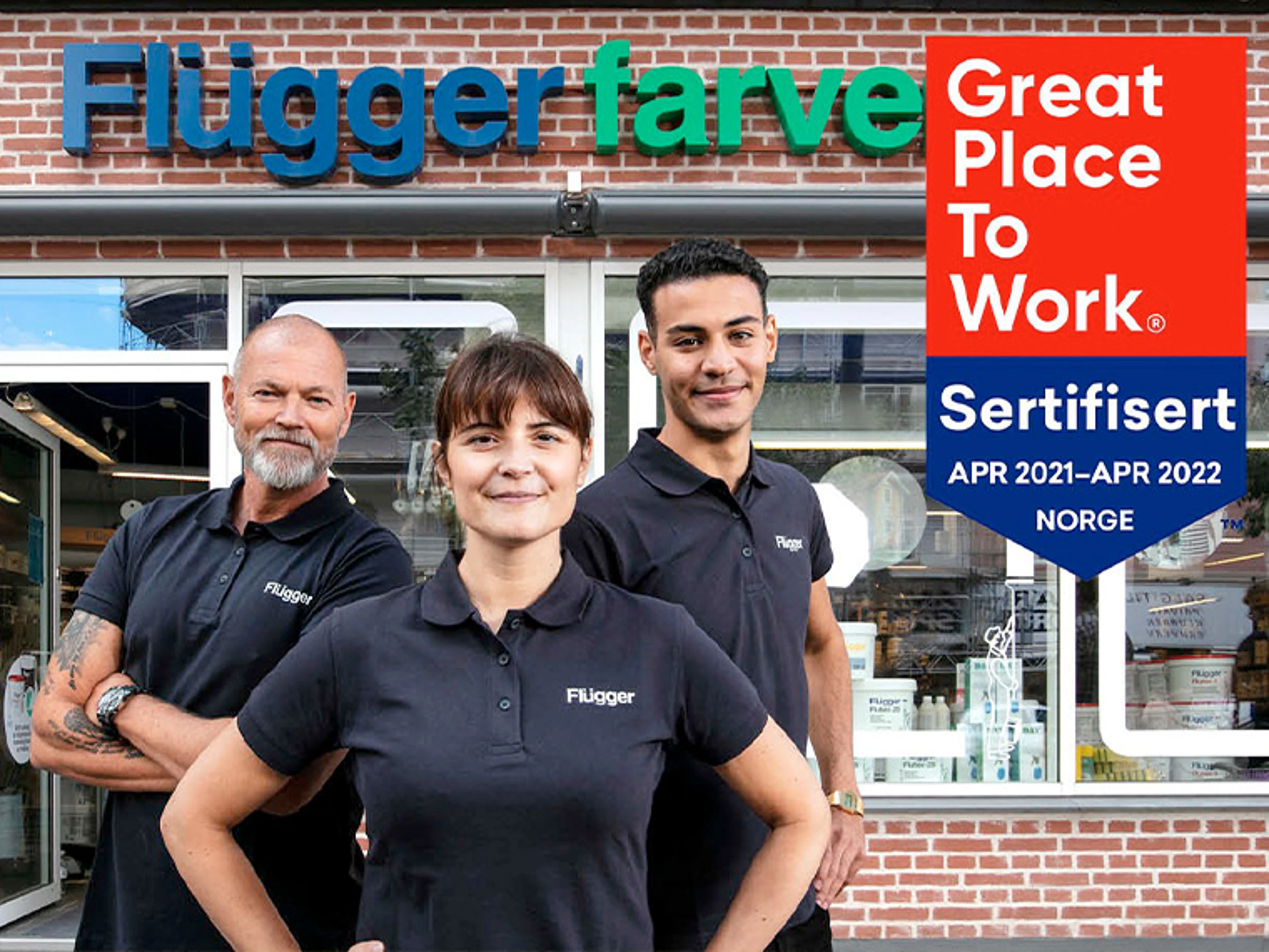 Tre Flügger-medarbejdere står foran en Flügger-butik med Flügger farve-skilt over indgangen. På billedet vises også mærket "Great Place to Work Certificeret Norge 2021-2022".