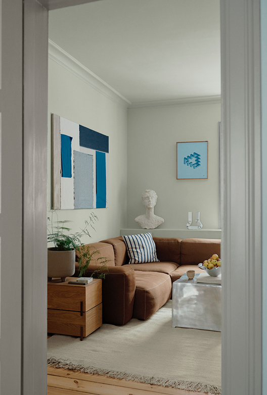 Stue set gennem en døråbning med lyse vægge, brun sofa, kunst og sofabord.