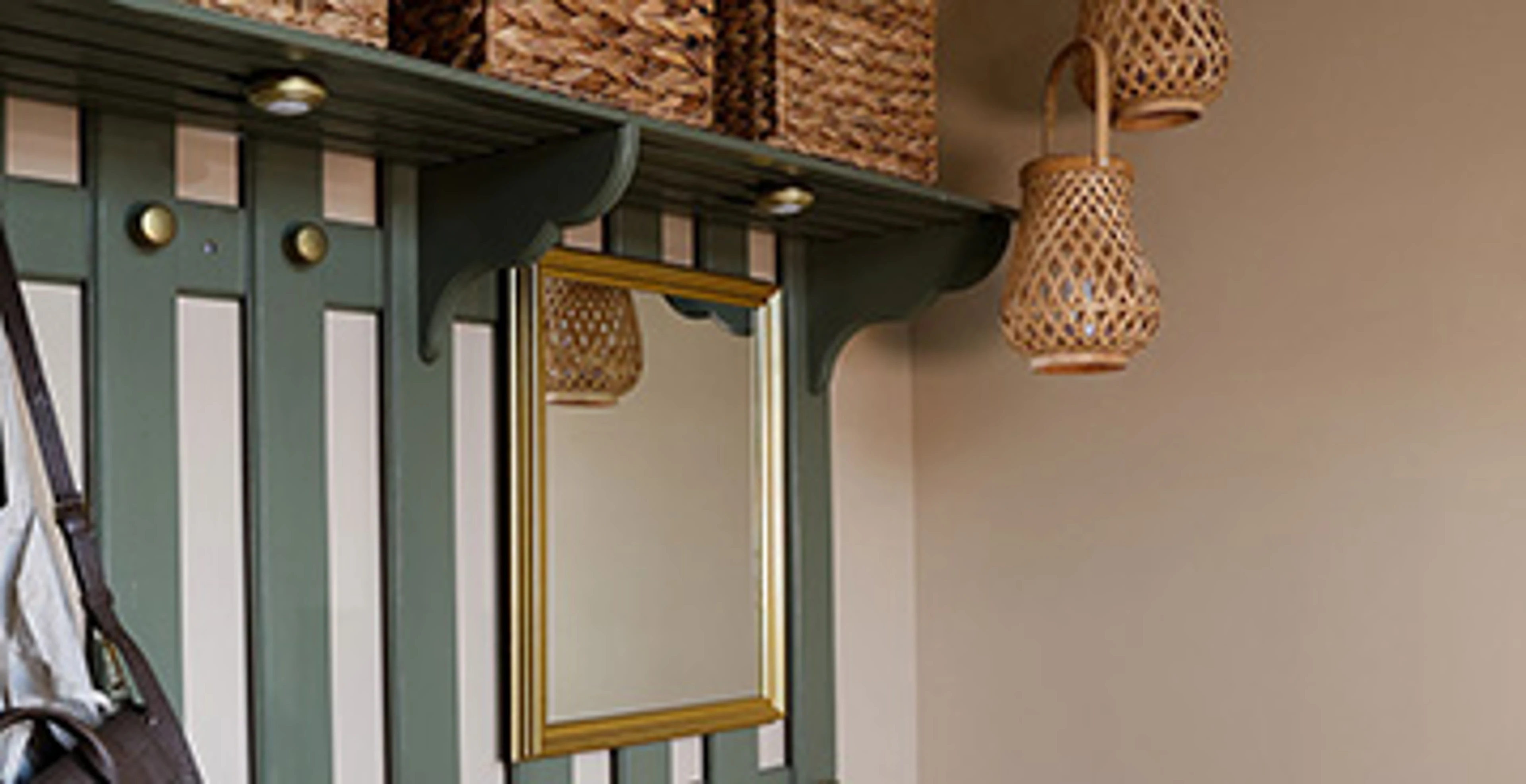 Garderobe med beige vægge, og en grøn knagerække med et spejl i guldramme. På hattehylden er der kurve i flettet materiale.