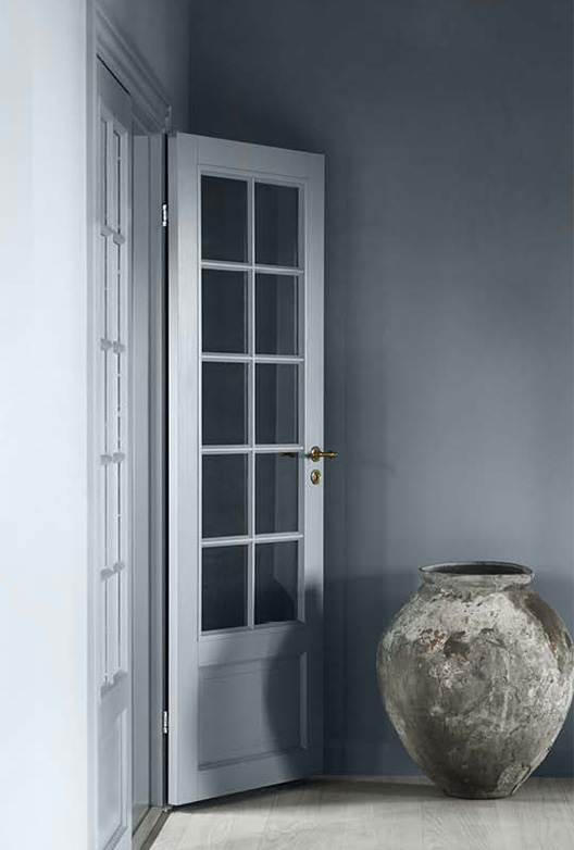Blågrå vegg med hvit dør med glassfelt og stor keramisk krukke.
