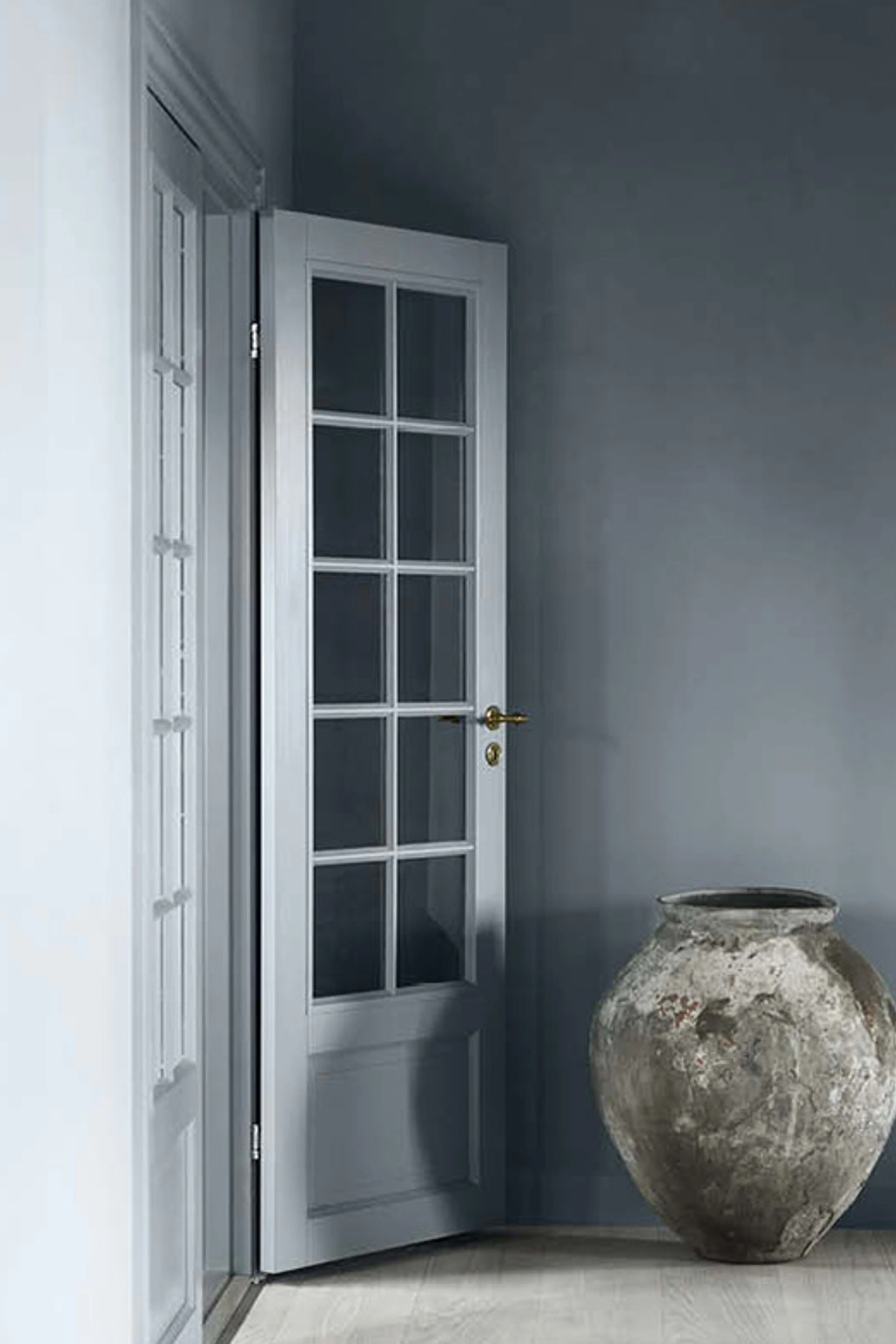 Blågrå vegg med hvit dør med glassfelt og stor keramisk krukke.