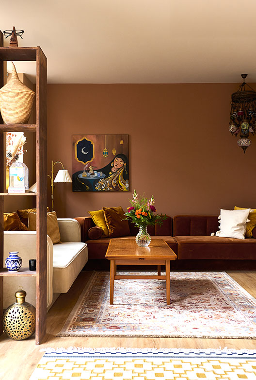 Warm living room with a brown wall, sofa, Oriental rug, wooden table, colorful cushions, and decorative art objects.
