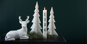 White ceramic Christmas trees, a reindeer figure and an Advent candle with countdown numbers on a dark green background.