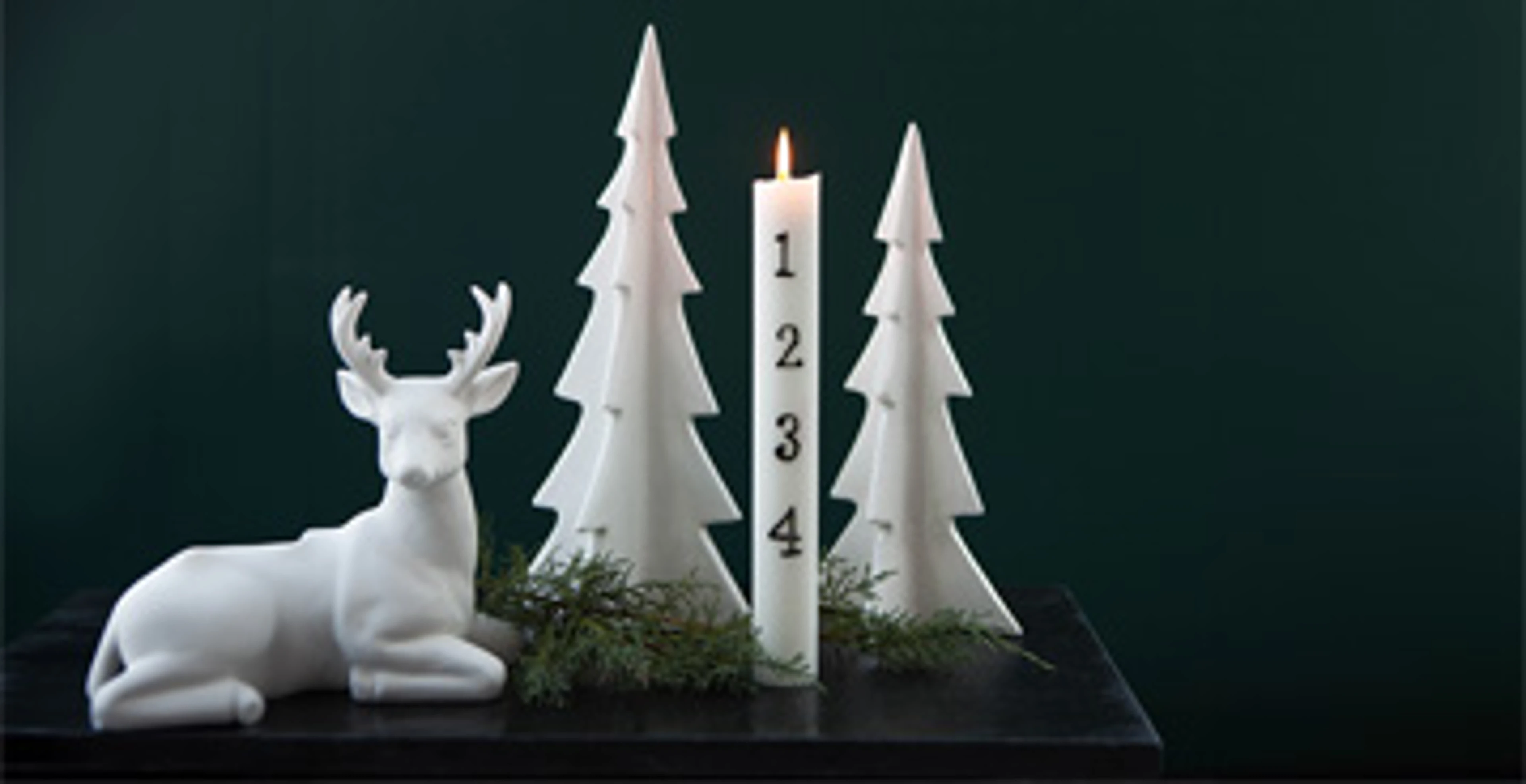 White ceramic Christmas trees, a reindeer figure and an Advent candle with countdown numbers on a dark green background.