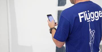 Maler i Flügger t-shirt med logo på ryggen holder mobiltelefon