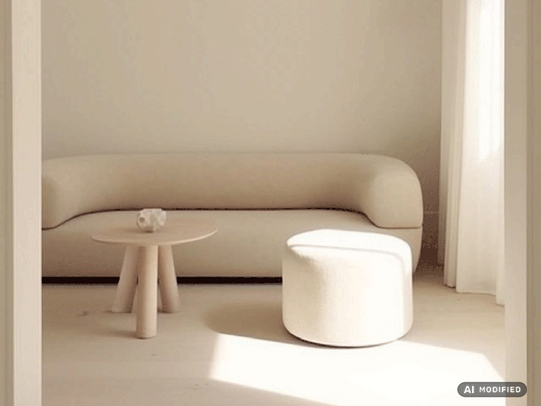 Lyst opholdsrum med vægge malet i Flügger-farven Cotton (FL8012). En buet sofa, en rund puf og et lille rundt bord i lyse nuancer er placeret i et minimalistisk interiør med blødt dagslys.