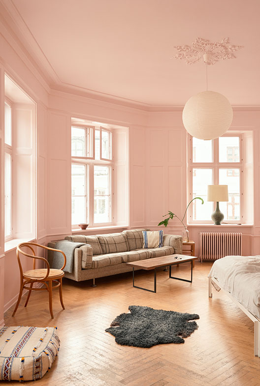 Lyst rosa soveværelse med sofa, seng og store vinduer