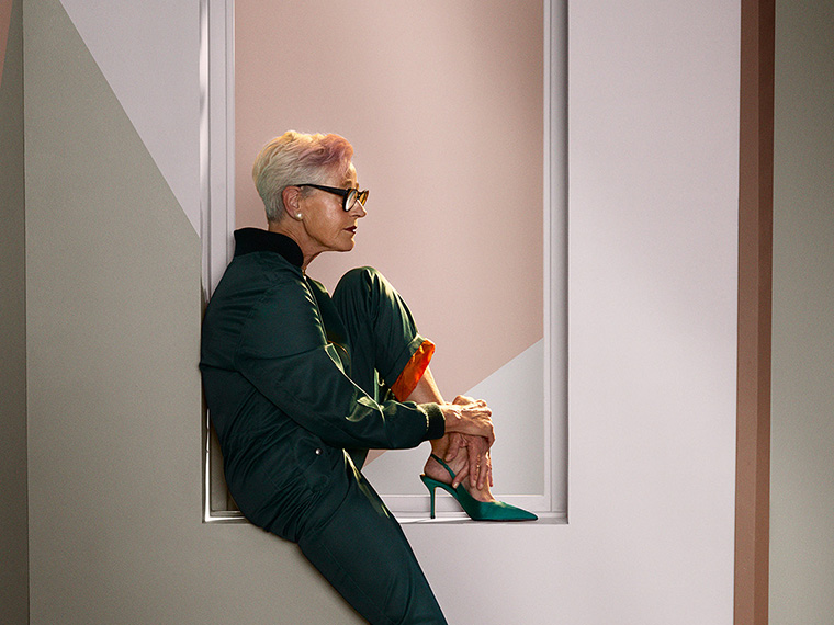 Person in dark clothing sits in a framed wall niche surrounded by walls with geometric colour blocks in beige, green and pink shades. The image highlights the interplay between colours, shapes and modern interior design.