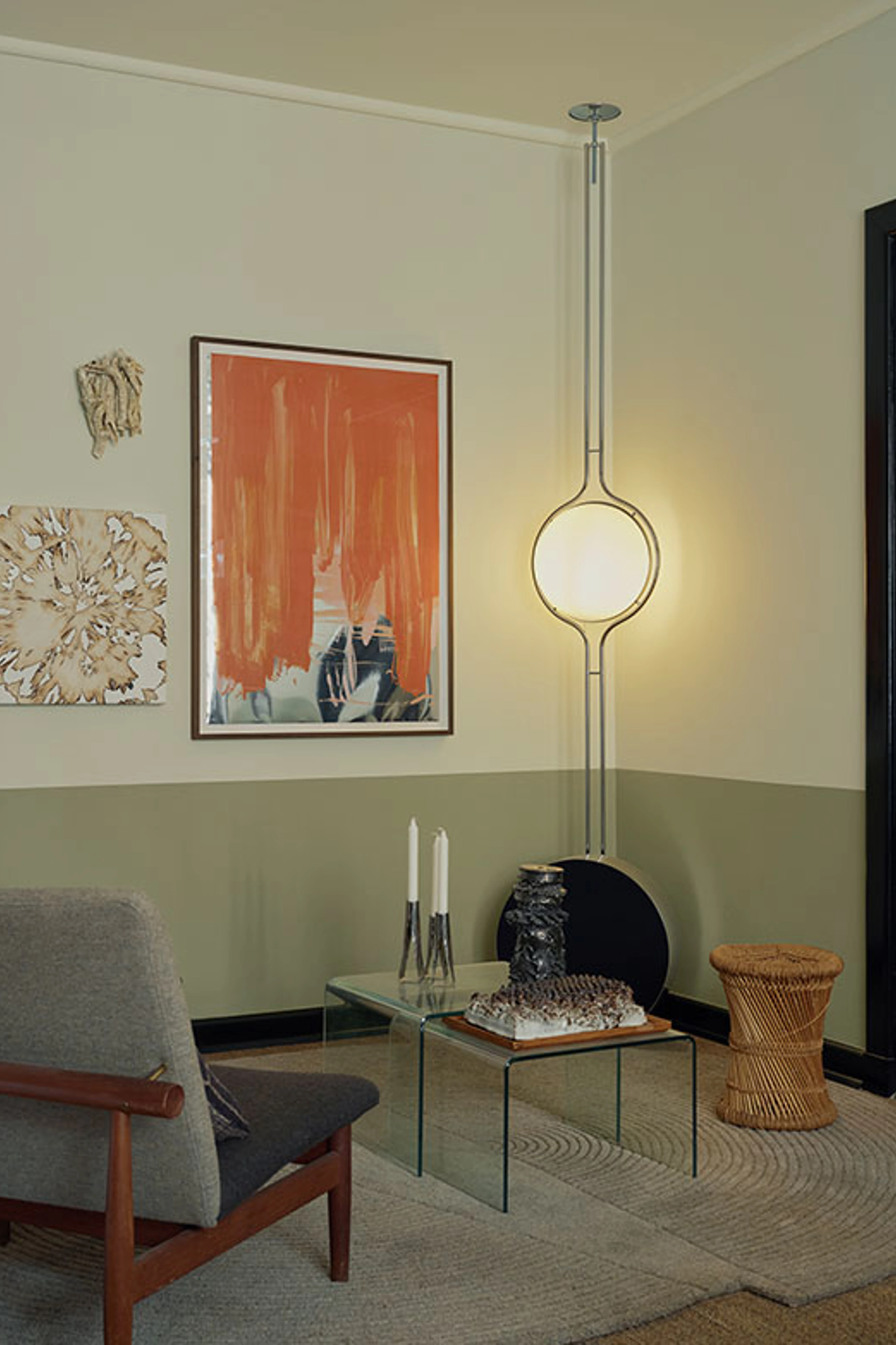 Living room corner with a gray armchair, glass table, artwork on the wall, and a sculptural floor lamp with a round light source.