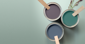 3 paint buckets of green, dark blue and pigalle colors with mixing sticks. Buckets placed at green background.