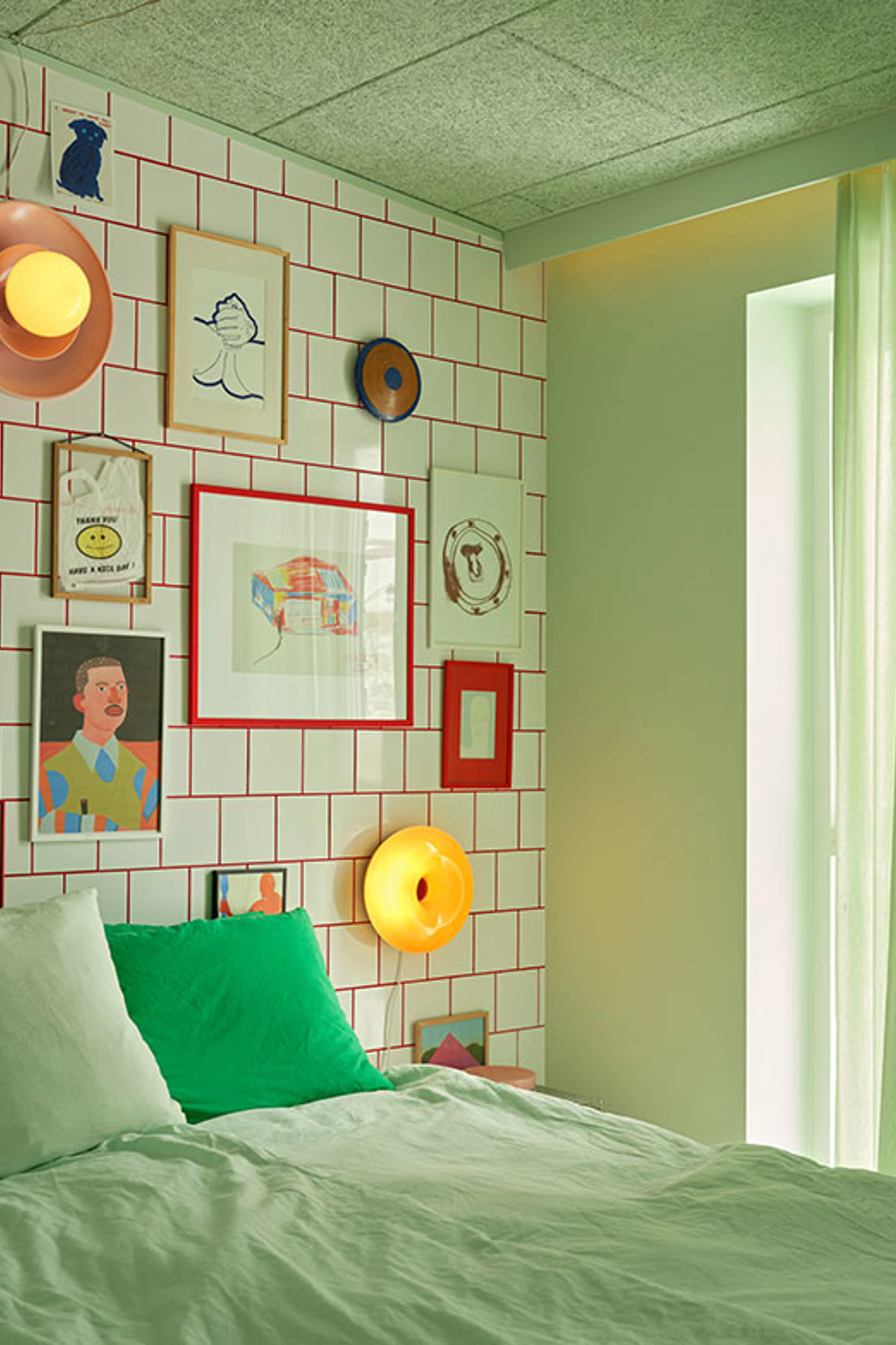 Bedroom with mint green textiles, a green cushion, and a gallery wall on white tiles with red grout.