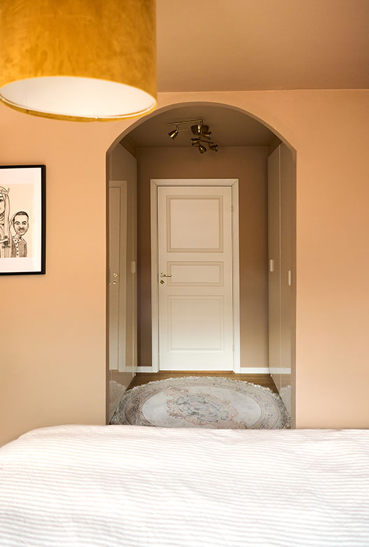 Bedroom with peach-colored walls and an arched opening leading to a muted gray-brown hallway with a white door.