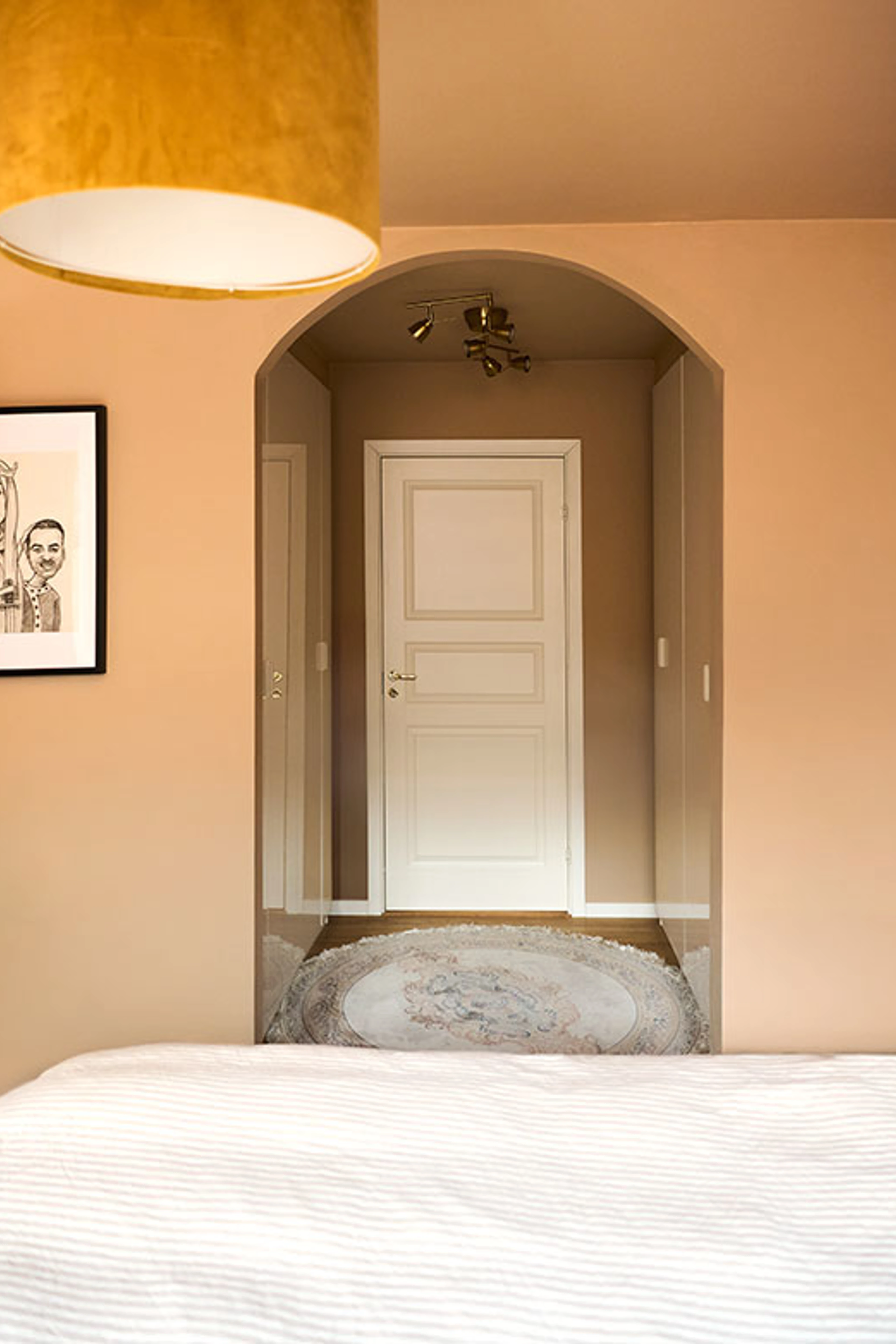 Bedroom with peach-colored walls and an arched opening leading to a muted gray-brown hallway with a white door.
