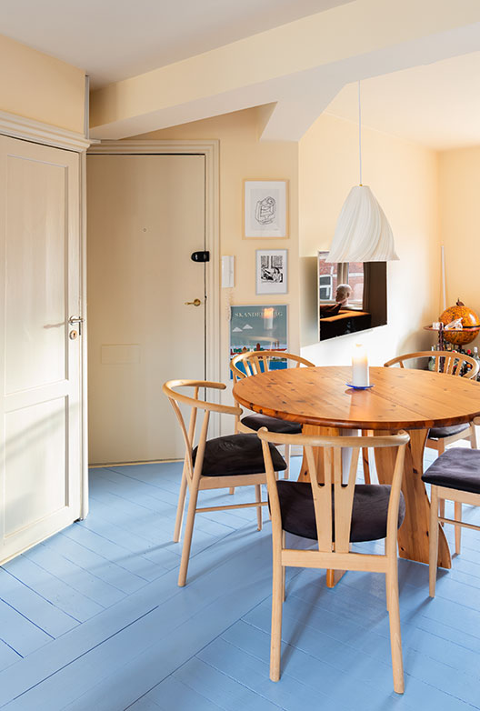 Rundt spisebord med træstole, pendellampe og lyseblåt gulv.