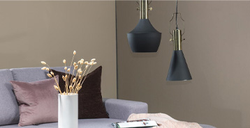 Et hjørne af en stue med en lys sofa, puder i rosa og mørke nuancer, en hvid vase med tørrede grene samt to mørkeblå pendellamper foran en beige væg.