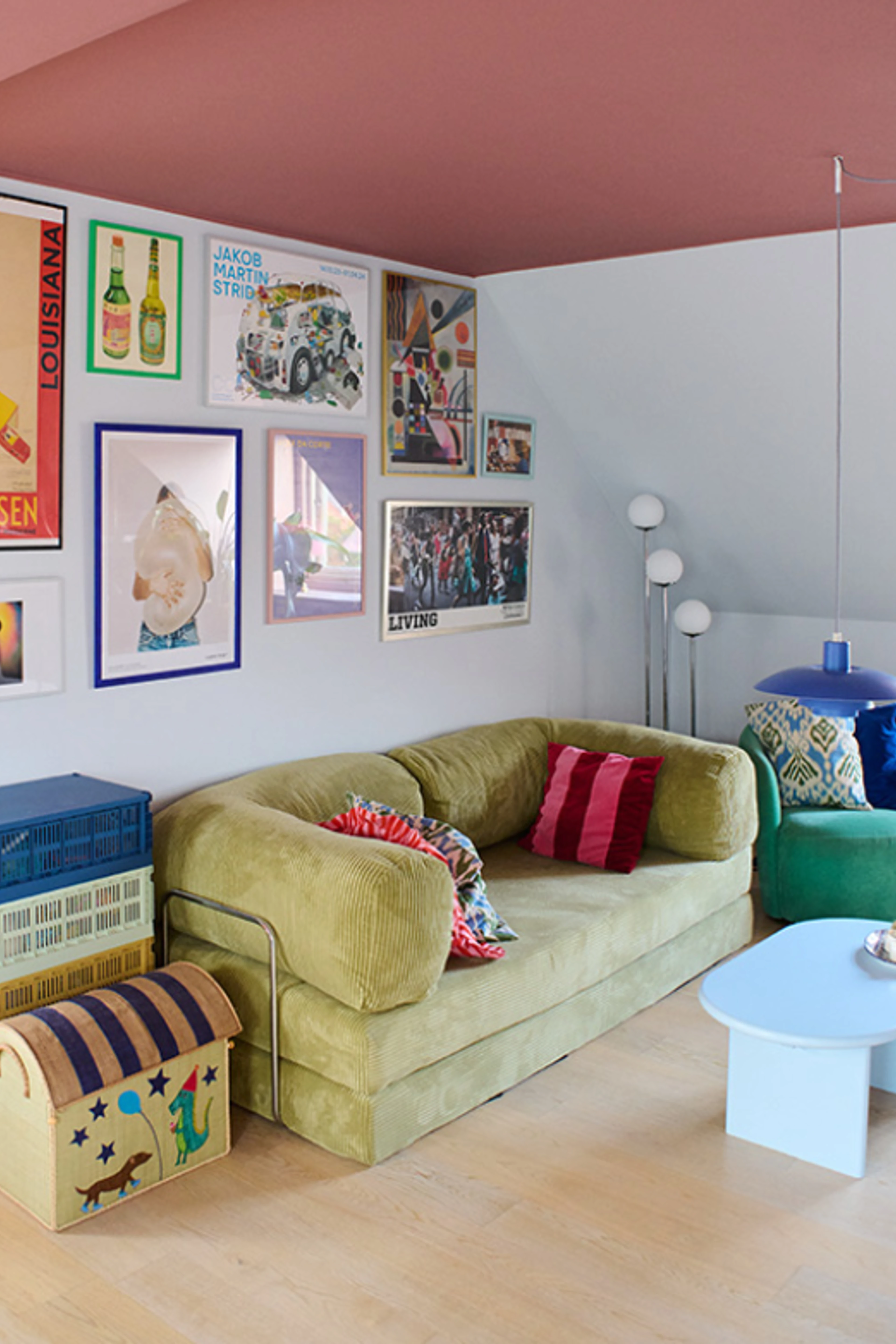 Stue med lyse vægge og rosa loft, indrettet med sofa, farverige puder, sofabord og væg med plakater.