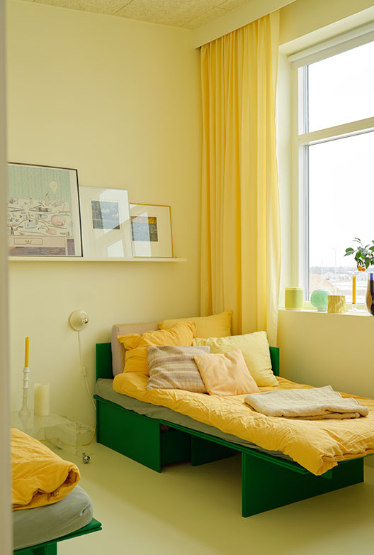 Sunny bedroom in shades of yellow and green, with a yellow bed, green bed frame, and long yellow curtains.