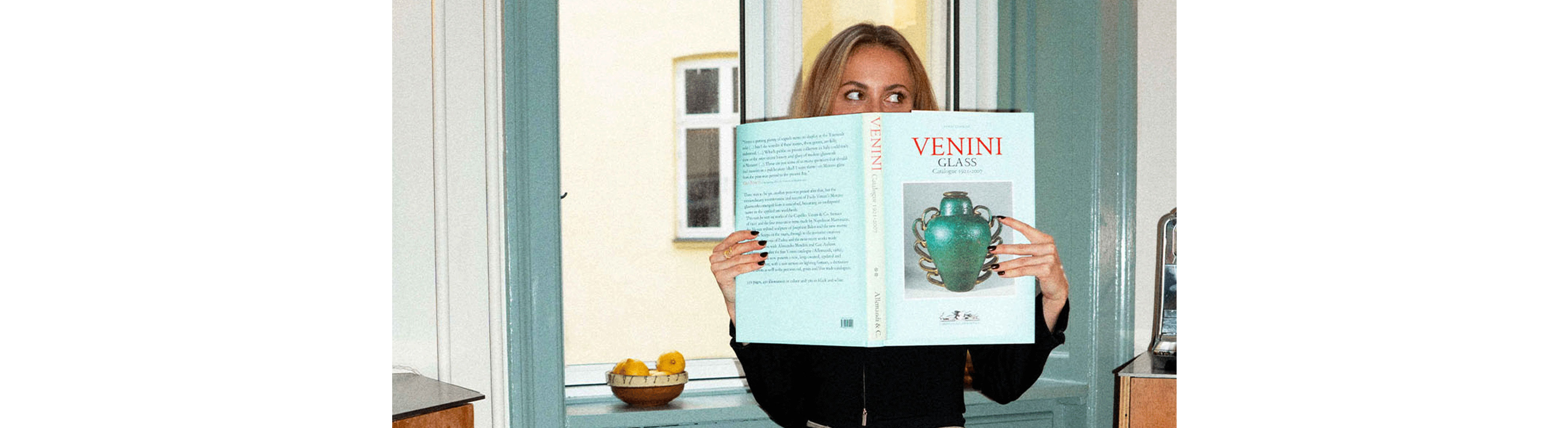 Frederikke står i en døråbning og læser en turkis bog, der matcher de malede paneler omkring hende.