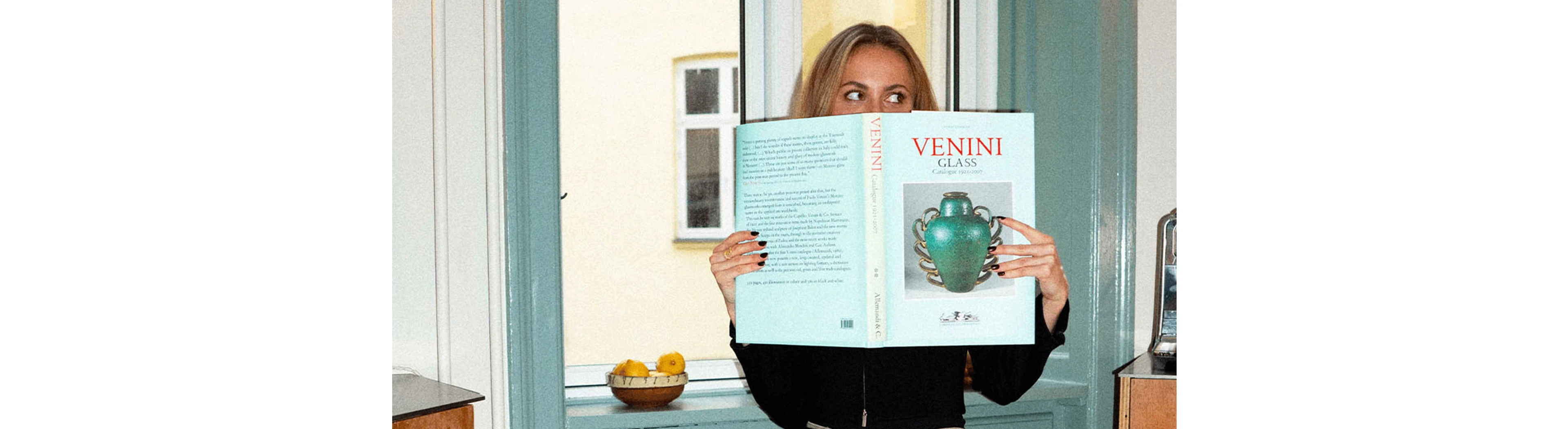 Frederikke står i en døråbning og læser en turkis bog, der matcher de malede paneler omkring hende.