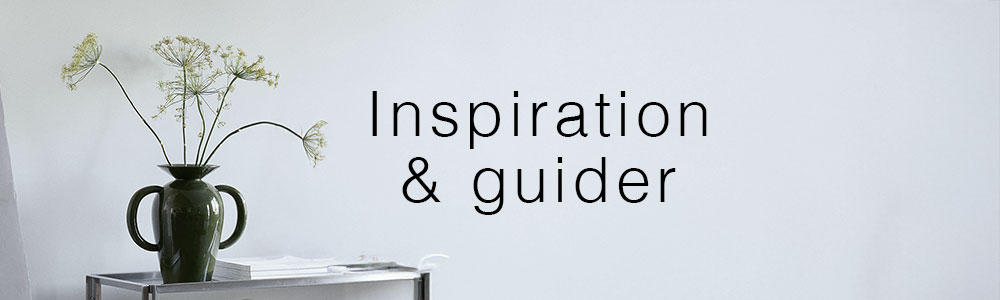 Vase med grønne blomster på et sidebord foran en lys væg med teksten "Inspiration & guider".