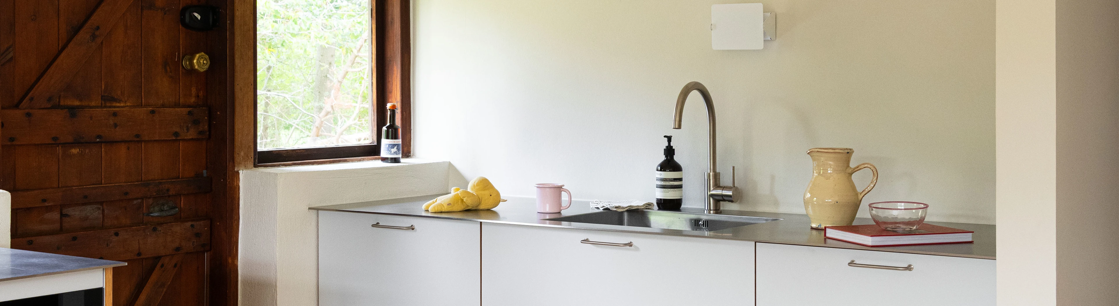 Kitchen with white walls, white cabinets, a steel worktop and an old wooden door.