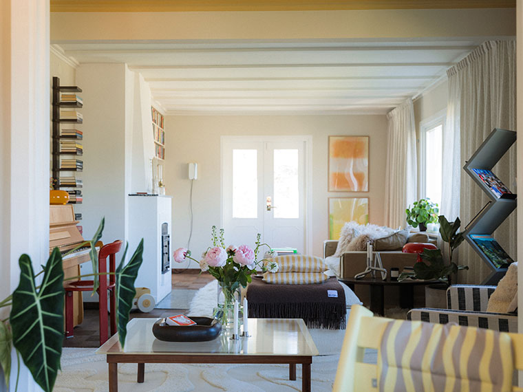 Living room with white ceiling beams, pink peonies and a piano in the background.