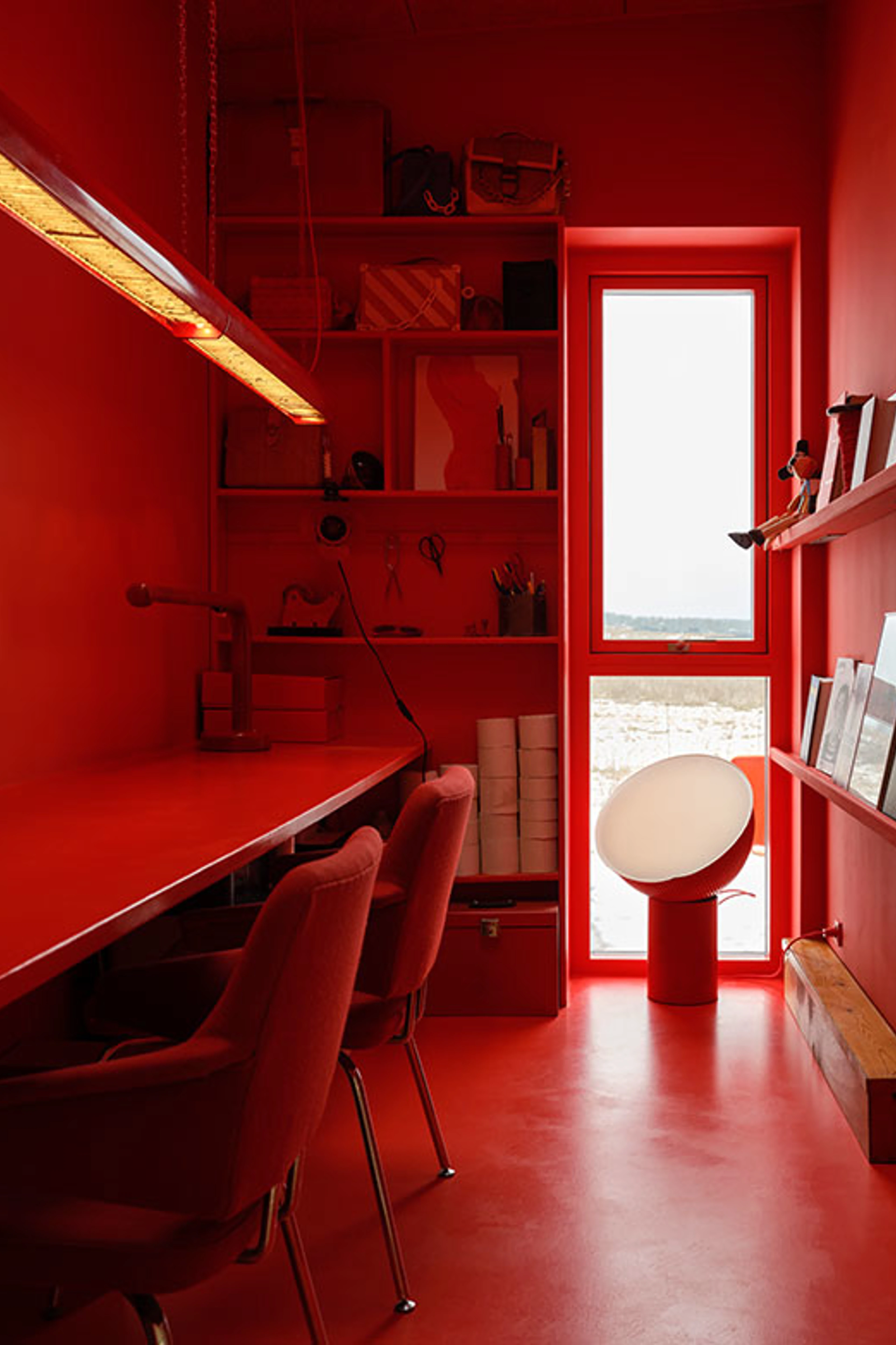 All-red home office with a long desk, red chairs, built-in shelves, and a narrow window.